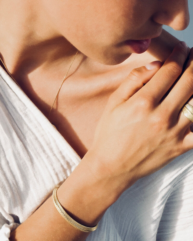 Der zierliche, goldene Armreif mit feiner Meeresstruktur auf der Oberfläche, glänzt durch Schlichtheit und erinnert dich sanft an deine schönen Tage am Meer