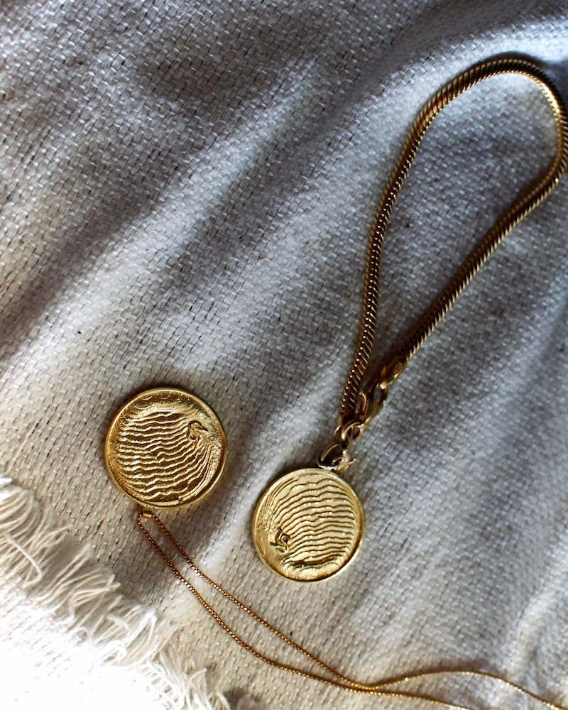 Das goldene Mirrow Necklace rückseitig mit feinsten maritimen Strukturen, eingefasst in einem glänzenden Rund. Dieses Amulett ist edel und zeitlos 