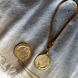 Das goldene Mirrow Necklace rückseitig mit feinsten maritimen Strukturen, eingefasst in einem glänzenden Rund. Dieses Amulett ist edel und zeitlos 